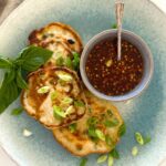 3 sourdough discard scallion pancakes sitting on a blue stoneware plate. There is also a bowl of chili soy dipping sauce sitting on the plate.