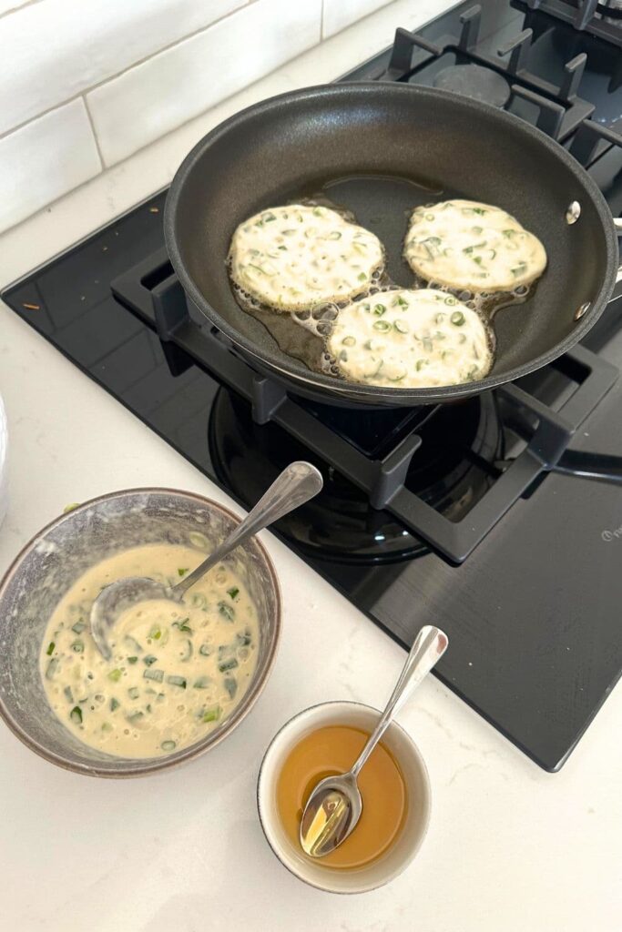 Sourdough discard scallion pancakes cooking in a non stick frying pan.