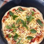 Sourdough pizza focaccia bread topped with tomato sauce, mozzarella and basil. The dough is sitting in a cast iron skillet.