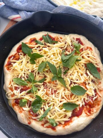 Sourdough pizza focaccia bread topped with tomato sauce, mozzarella and basil. The dough is sitting in a cast iron skillet.
