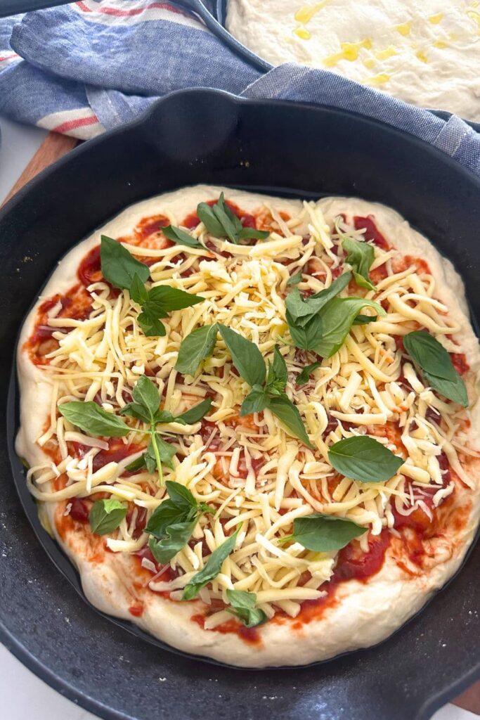 Sourdough pizza focaccia bread topped with tomato sauce, mozzarella and basil. The dough is sitting in a cast iron skillet.