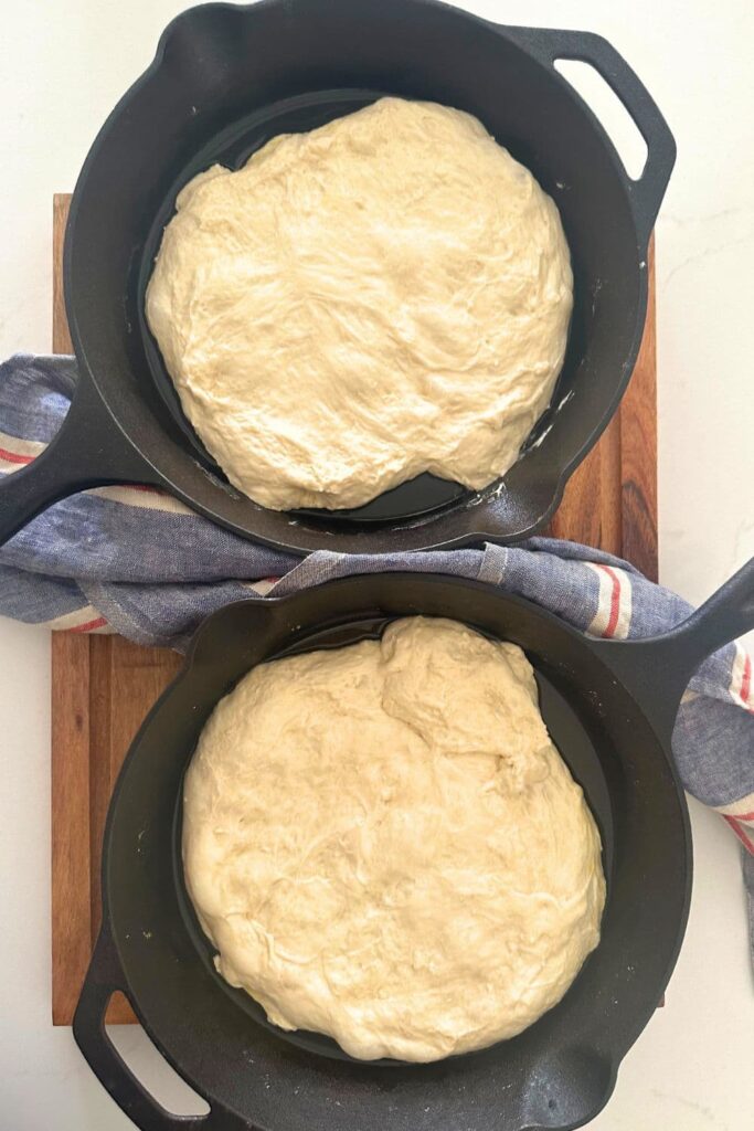 2 cast iron skillets filled with sourdough pizza focaccia dough.