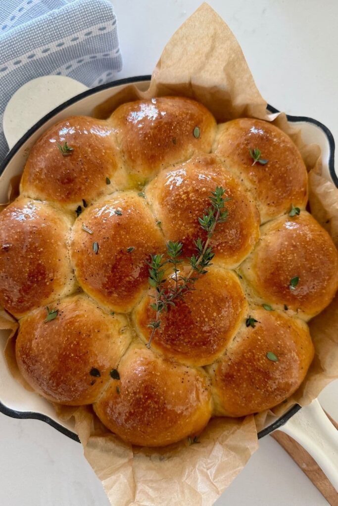 An enamel cast iron skillet filled with sourdough discard rolls topped in honey thyme butter. 