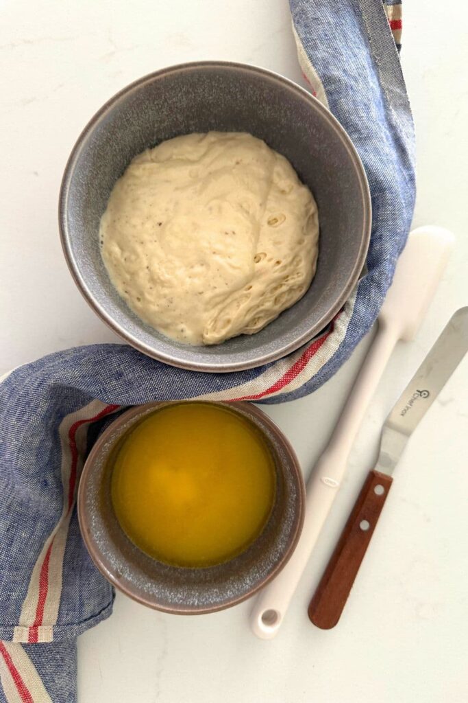 A bowl of sourdough discard sitting next to a bowl of melted butter to make sourdough crackers with no added flour.