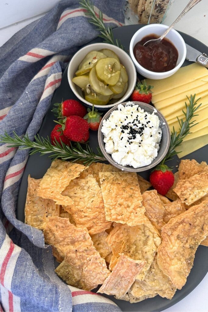 A colorful charcuterie platter featuring sourdough discard crackers with no added flour, as well as some feta cheese, pickles, cheese slices, relish and strawberries.