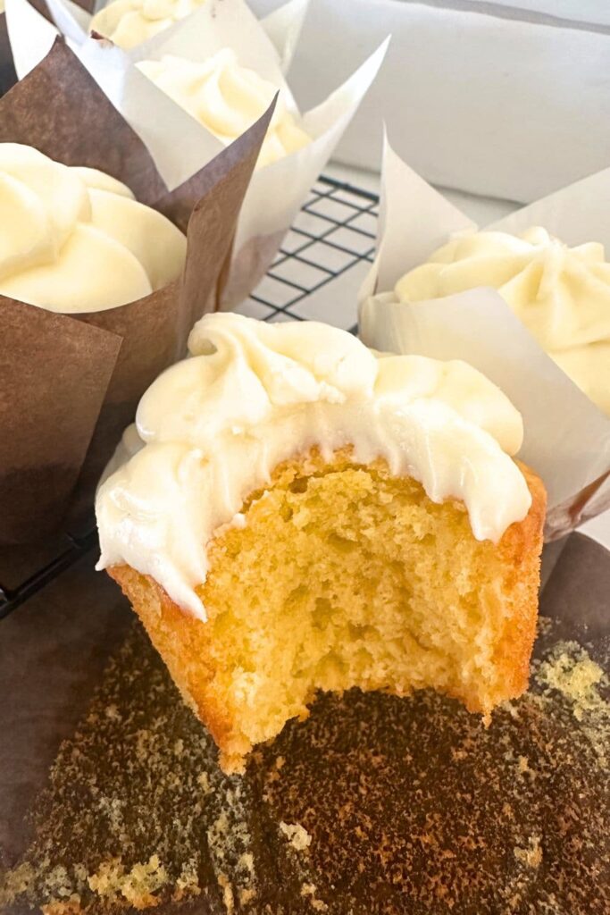 A sourdough vanilla cupcake that has been bitten into to show the buttery, tender crumb. The cupcake has been frosted in vanilla cream cheese frosting.