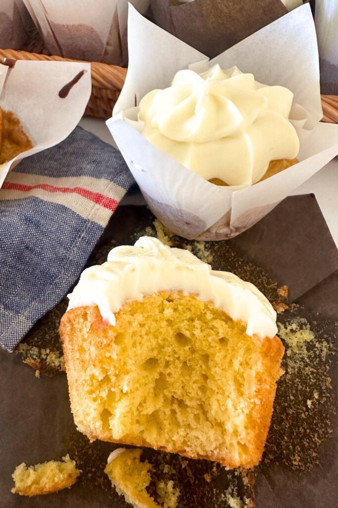 A sourdough vanilla cupcake that has been bitten into so you can see the moist, buttery crumb inside. 