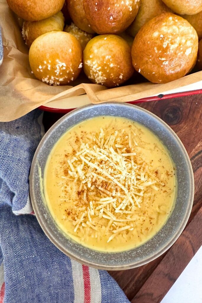 Golden baked sourdough discard pretzel bites served in an enamel tray. There is also a small dish of 3 ingredient beer cheese dip next to the tray and you can see a blue linen dish towel in the photo too.