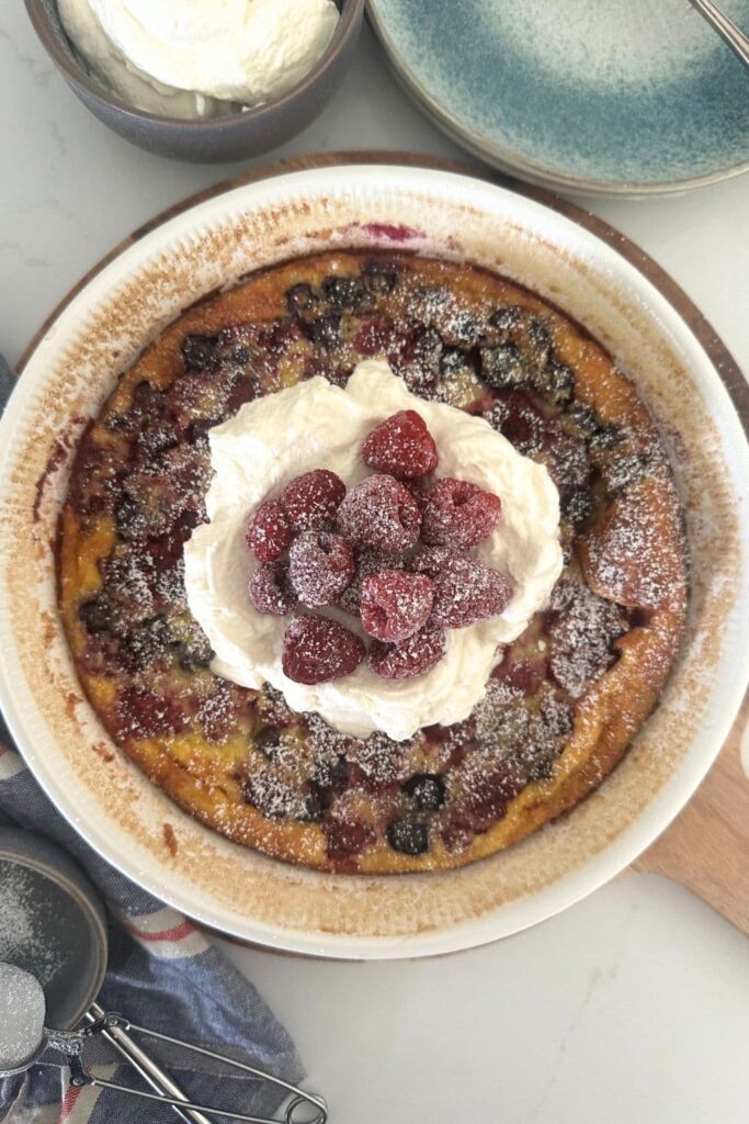 A mixed berry sourdough clafoutis baked in a pie dish and topped with whipped cream and raspberries.