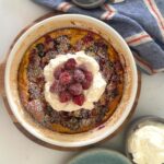 Sourdough berry clafoutis topped with whipped cream and fresh raspberries.