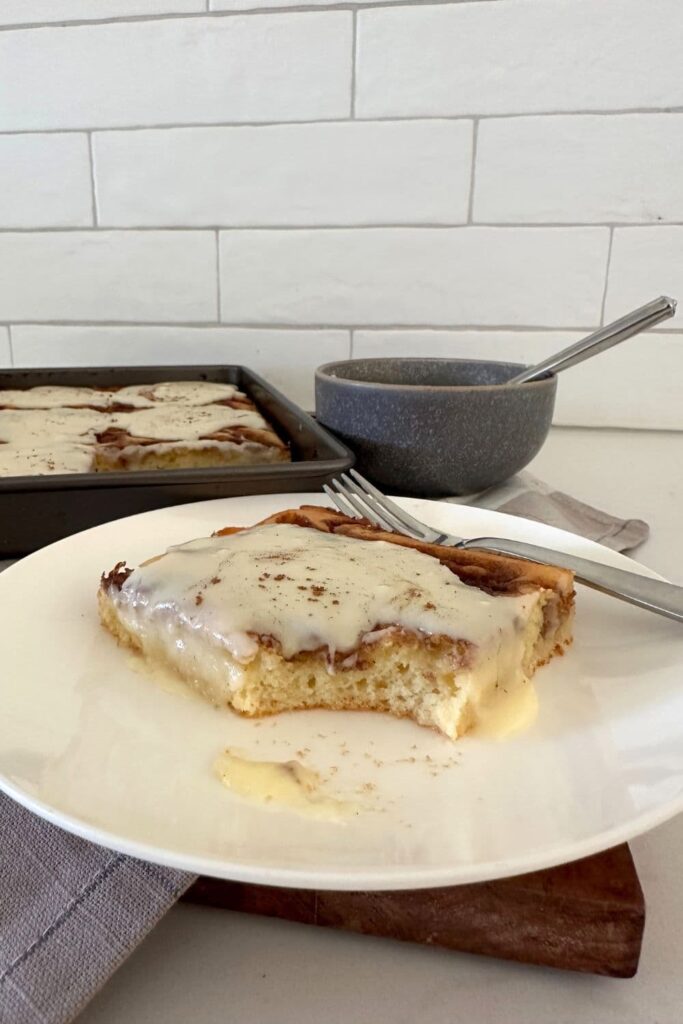 Close up photo of a slice of baked sourdough cinnamon roll pancake drizzled with icing. You can see the fluffy interior of the sourdough pancake.