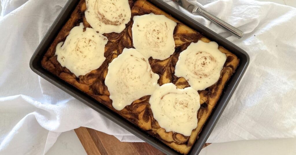 A tray of sourdough cinnamon roll pancakes baked in a sheet pan and topped with creamy vanilla icing.