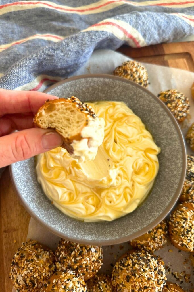 A bowl of honey cream cheese dip swirled with raw honey. The bowl is surrounded by sourdough bagel bites coated in everything bagel seasoning.