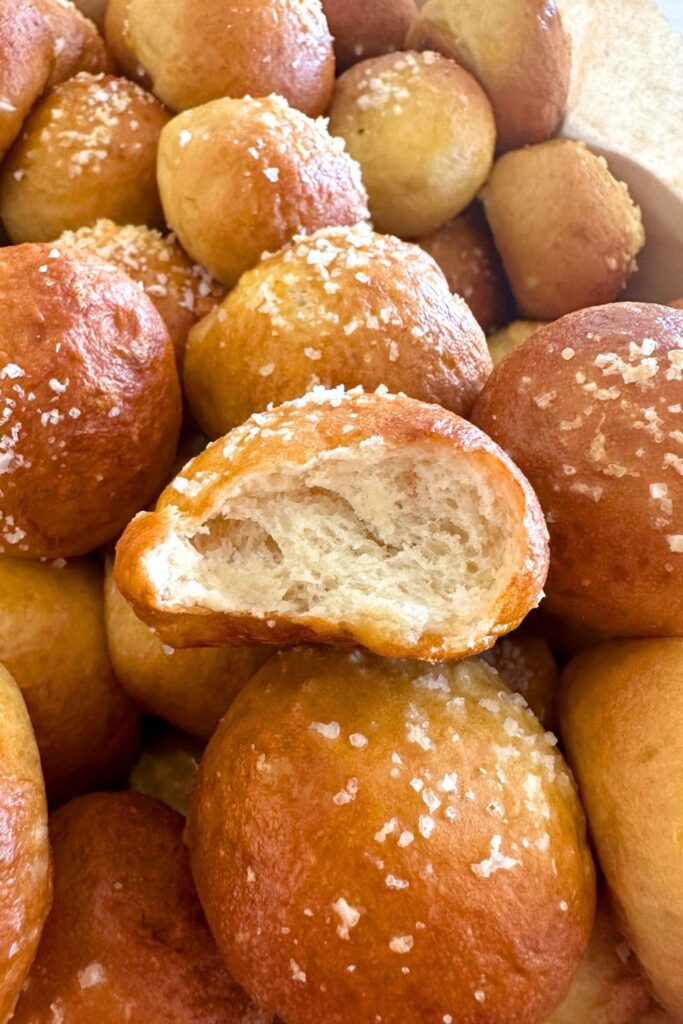 Close up photo of a sourdough discard pretzel bite. Someone has taken a bit and you can see the soft, chewy crumb of the interior. The other sourdough pretzel bites have been sprinkled in salt.