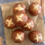 7 sourdough pretzel buns arranged on a sheet of parchment paper.