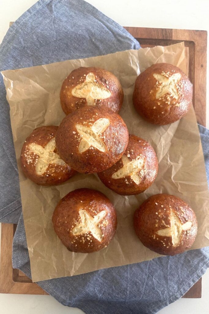 7 sourdough pretzel buns arranged on a sheet of parchment paper.