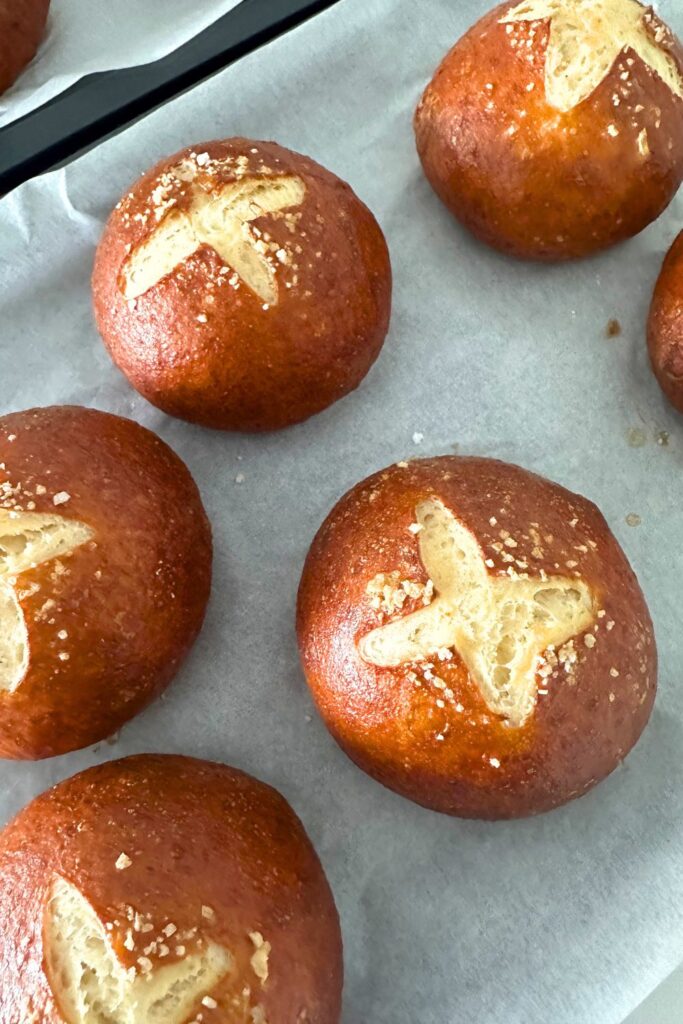 Sourdough pretzel buns sitting on a parchment lined cookie sheet.