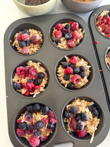 A 6 muffin hole tin filled with sourdough discard oatmeal breakfast cups topped with frozen berries and chia seeds.