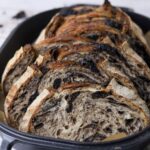 A loaf of cookies and cream sourdough bread that has been sliced and displayed inside a cast iron bread pan.