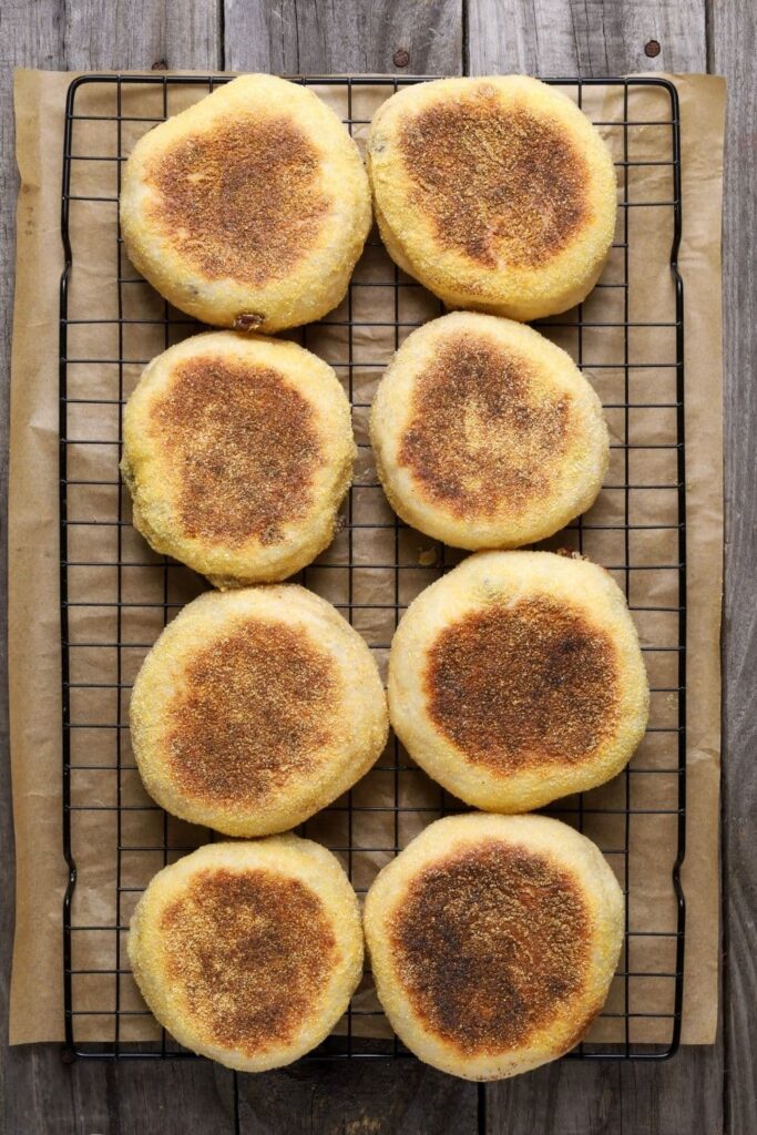 Sourdough discard cinnamon raisin English muffins on a cooling rack sitting over a piece of parchment paper.