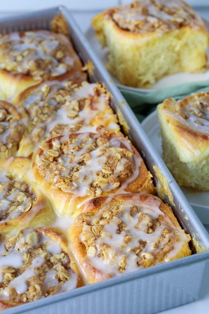 Sourdough apple cinnamon rolls in baking dish next to two plated cinnamon rolls.