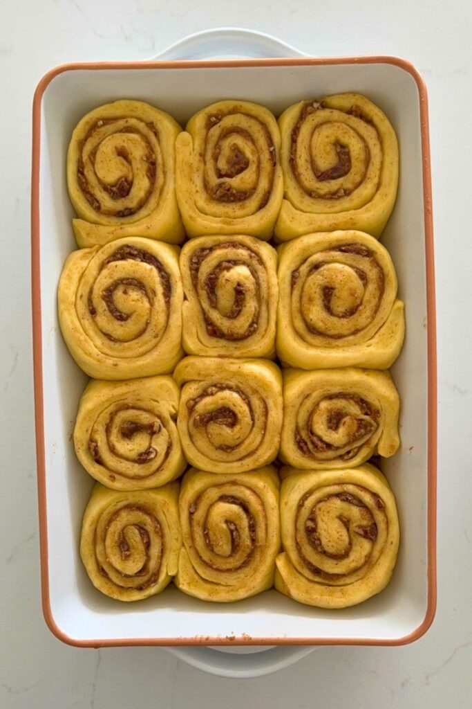 Sourdough maple pecan roll dough sliced in baking dish after second rise.