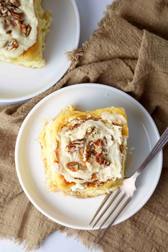 Sourdough maple pecan roll with glaze and chopped pecans on top, on a plate with a fork.