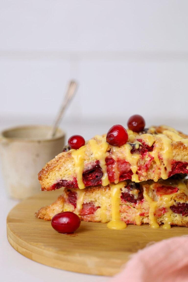 Sourdough orange cranberry scones stacked on wooden plate with fresh cranberries on top.