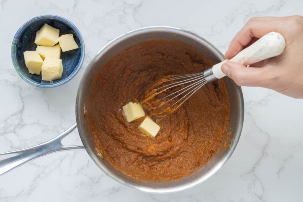 Adding cubes of butter to pumpkin butter with a whisk.