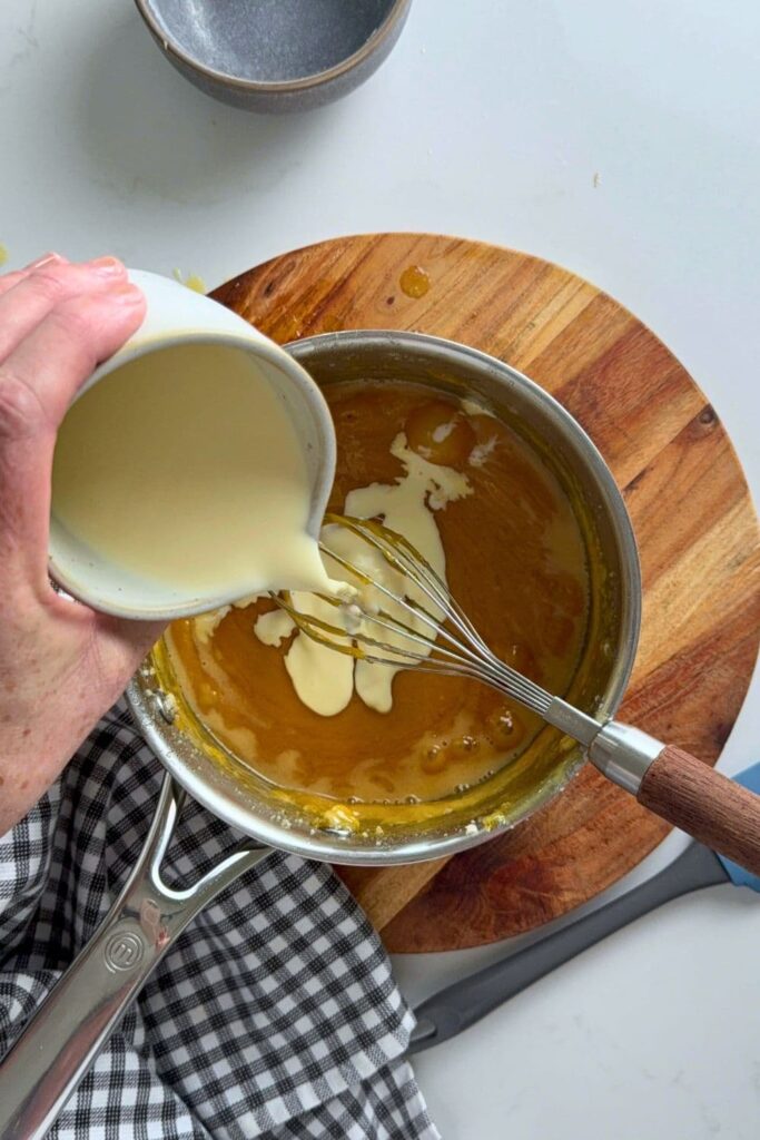 Pouring a jug of heavy whipping cream into a saucepan caramel sauce.