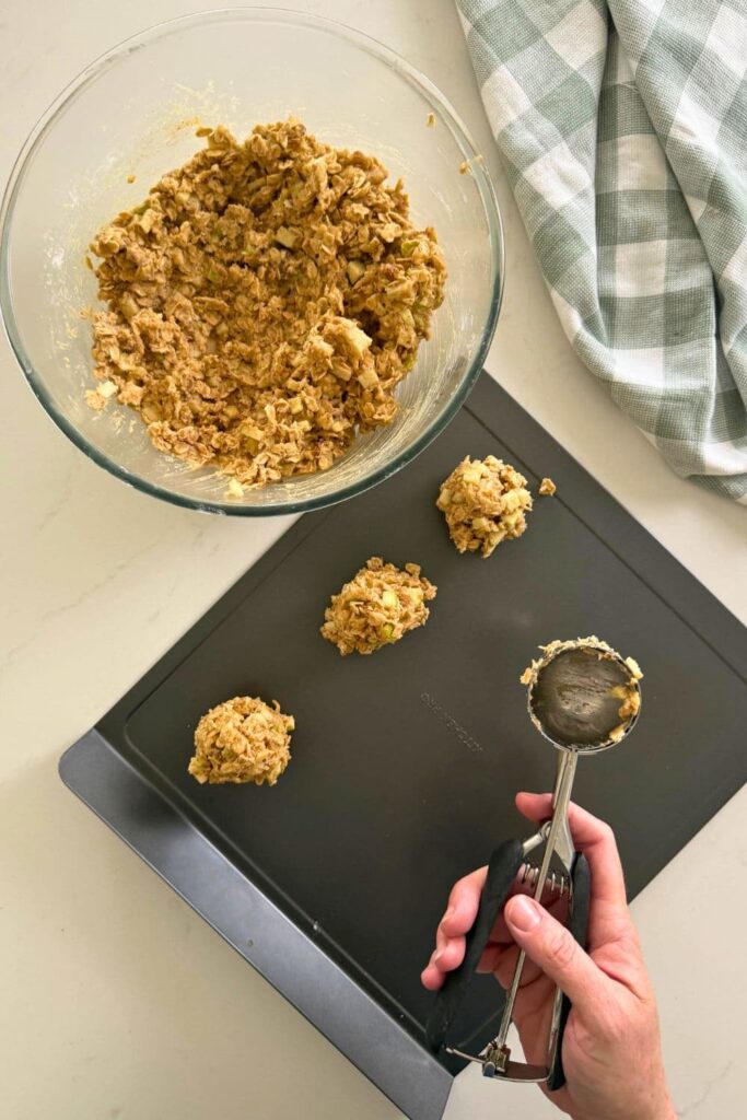 Scooping cookie dough out of a bowl and onto a cookie sheet to make apple cinnamon sourdough oatmeal cookies.