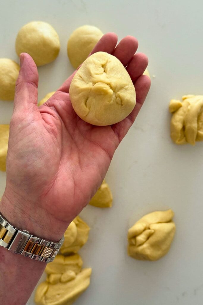 A hand holding a piece of sourdough honey butter roll dough.