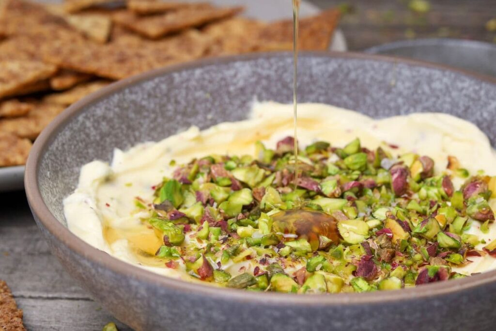 Honey pistachio cream cheese dip in a bowl with honey being drizzled on.
