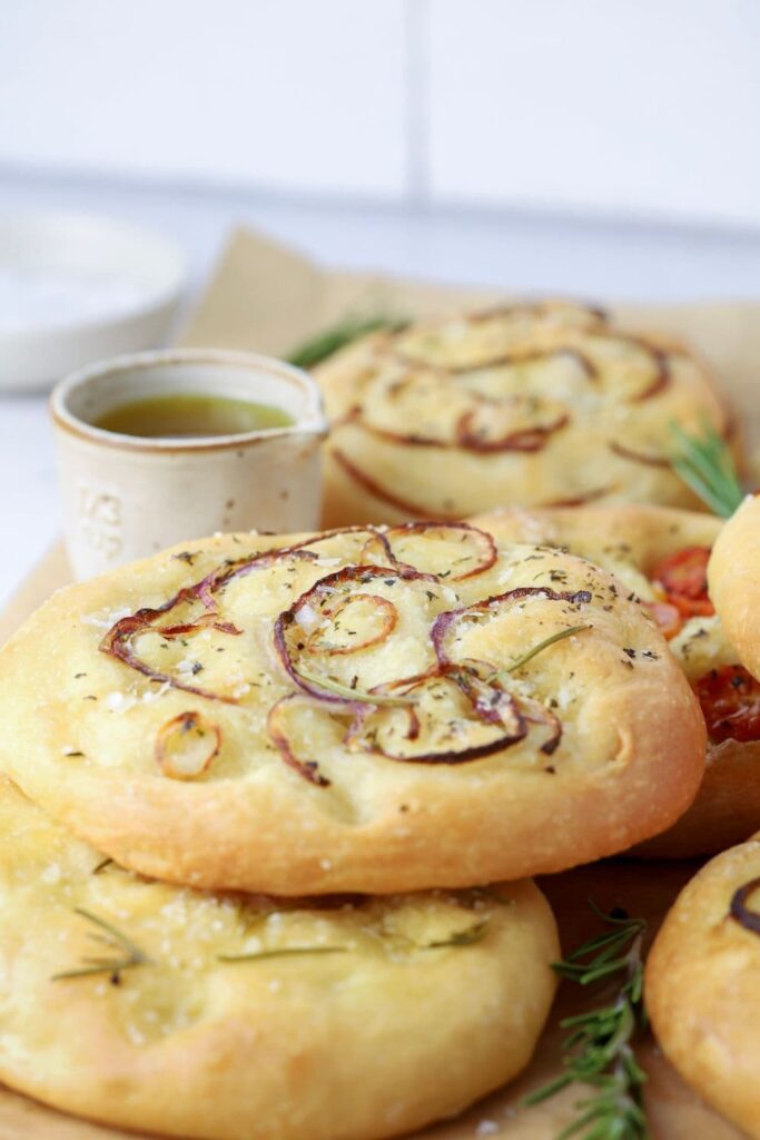 Baked sourdough focaccia rolls on parchment paper with a small dipping bowl of olive oil.