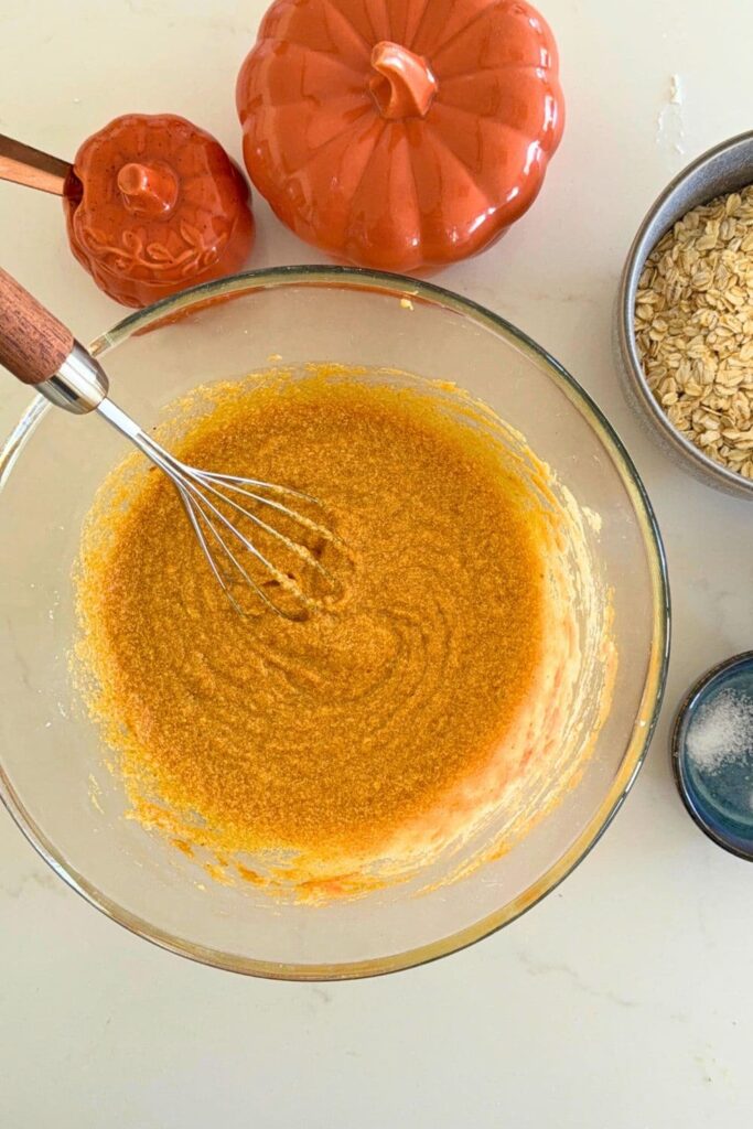 Mixing the wet ingredients with a whisk in a bowl to make a sourdough oatmeal pumpkin cookie skillet.