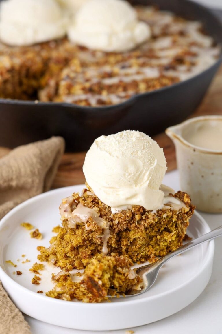 Close up of a slice of sourdough oatmeal pumpkin cookie skillet on a plate with a fork taking a bite and a scoop of vanilla ice cream on top.
