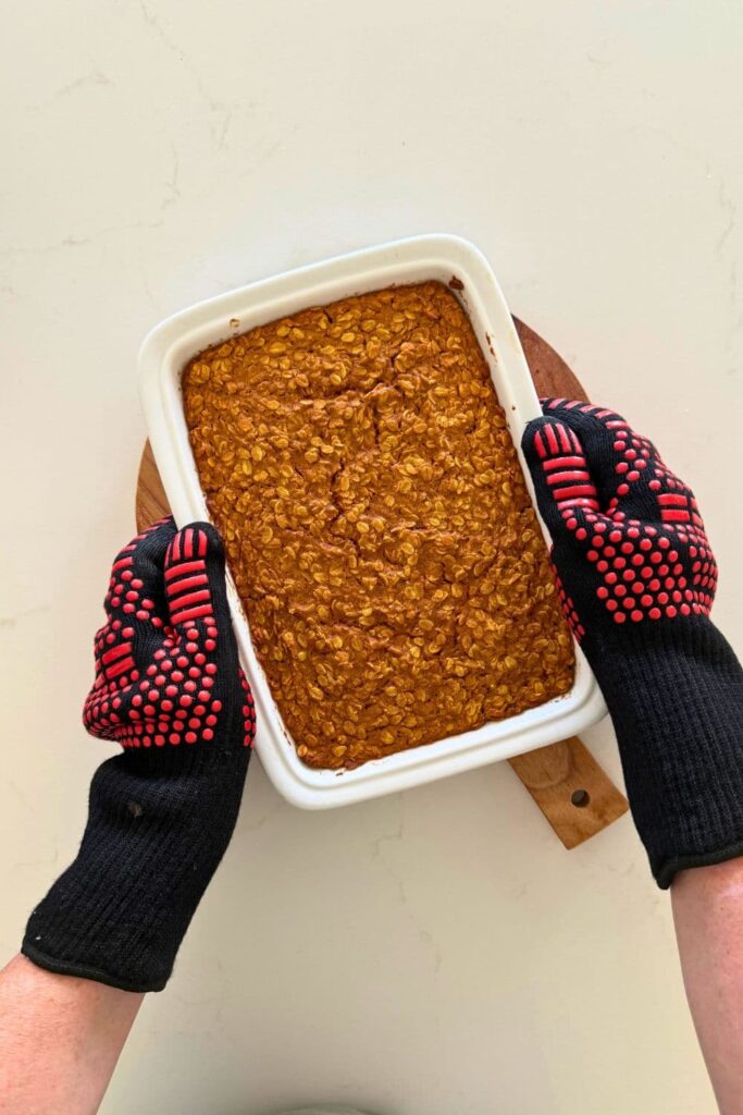 Hands with protective gloves on holding a baking dish with sourdough pumpkin pie baked oatmeal fresh out of oven.