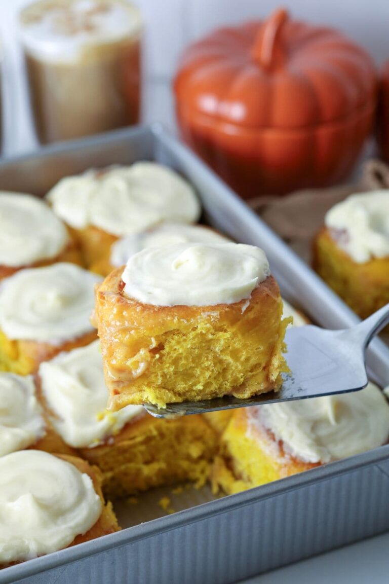 An image showing sourdough pumpkin sourdough rolls wtih cream cheese frosting with one being lifted up with a slice.