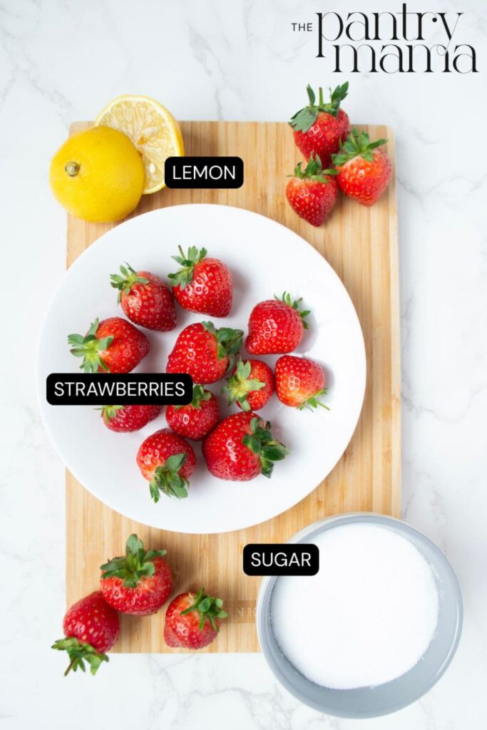 Flat lay of ingredients necessary to create easy strawberry jam with no pectin. There are strawberries, a lemon and a bowl of granulated sugar.