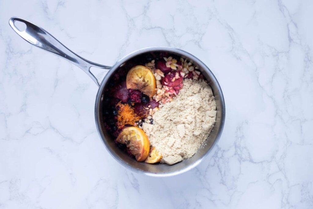 A small saucepan filled with oranges, berries, sugar and spices ready to make mulled berry jam.