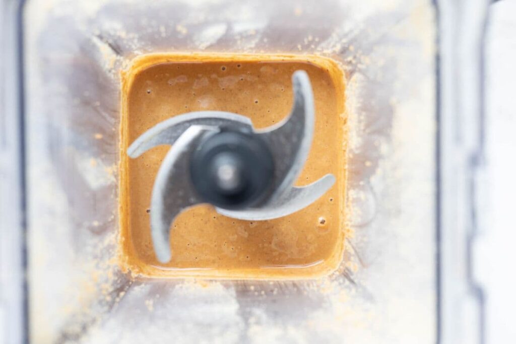 View of the inside of the blender to show roasted hazelnuts being blended into a nut butter to make homemade Nutella.