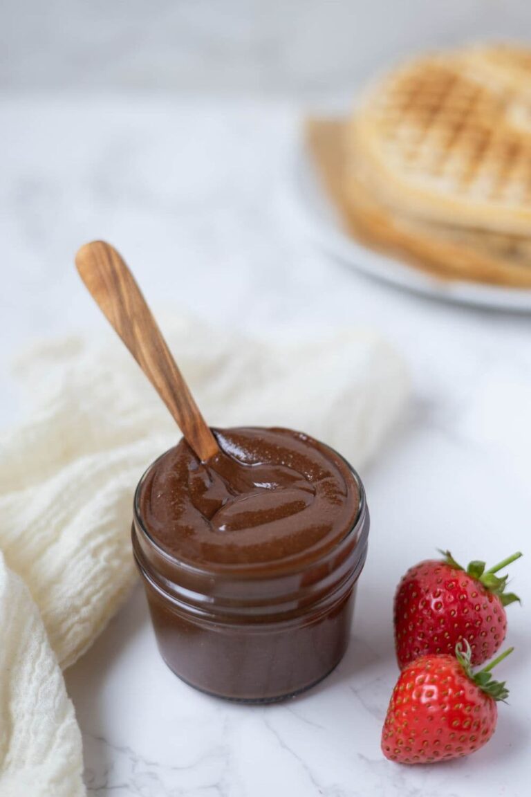 A jar of homemade Nutella on counter next to strawberries with sourdough waffles in the background.