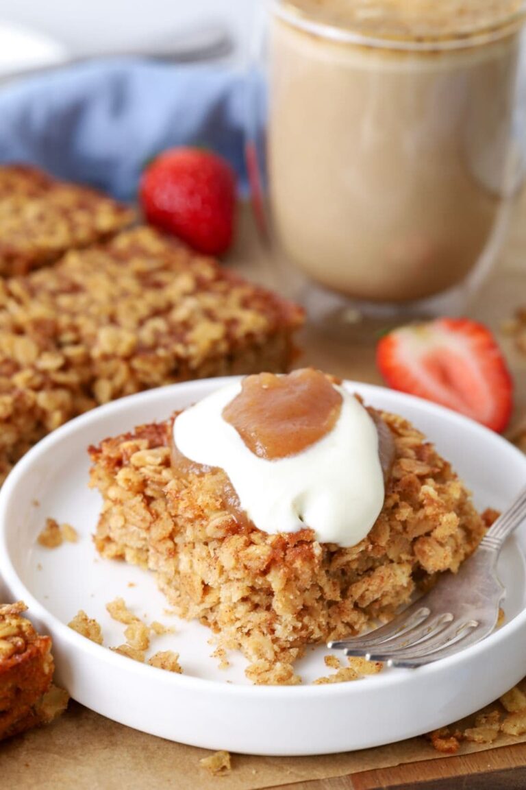 A slice of sourdough baked oatmeal on a plate topped with yogurt and apple butter for serving.