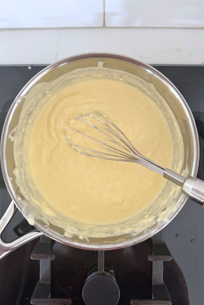 Whisking sour cream and cream cheese in a saucepan to make a sourdough cheese and garlic cobb loaf dip.
