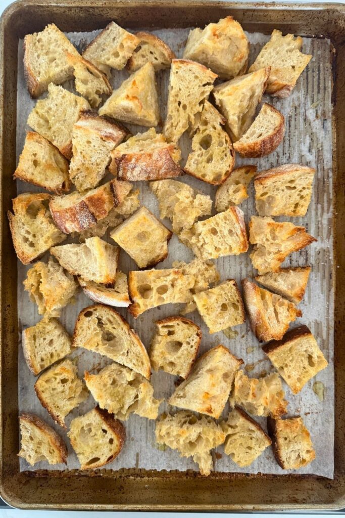 Toasting sourdough bread pieces on a baking sheet to eat with a sourdough cheese and garlic cobb loaf dip.