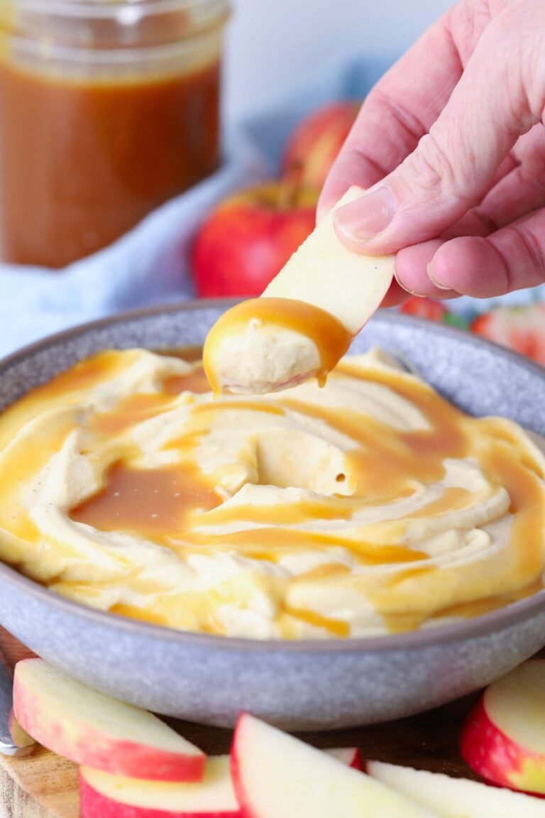 Hand dipping an apple slice into a bowl of whipped caramel dip.