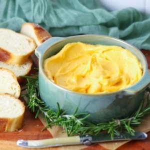 Cheddar butter being served in a bowl on a serving board with slices of sourdough bread.