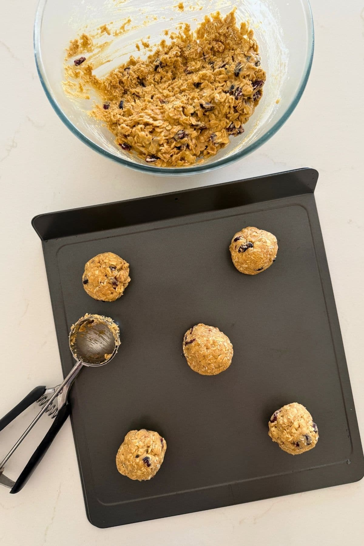 Scooping cookie dough balls on a cookie sheet to make orange cranberry sourdough oatmeal cookies.